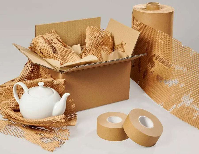 an unrolled roll of Grip Paperflex honeycomb paper beside a cardboard box filled with items wrapped in honeycomb paper and a teapot nestled in honeycomb paper