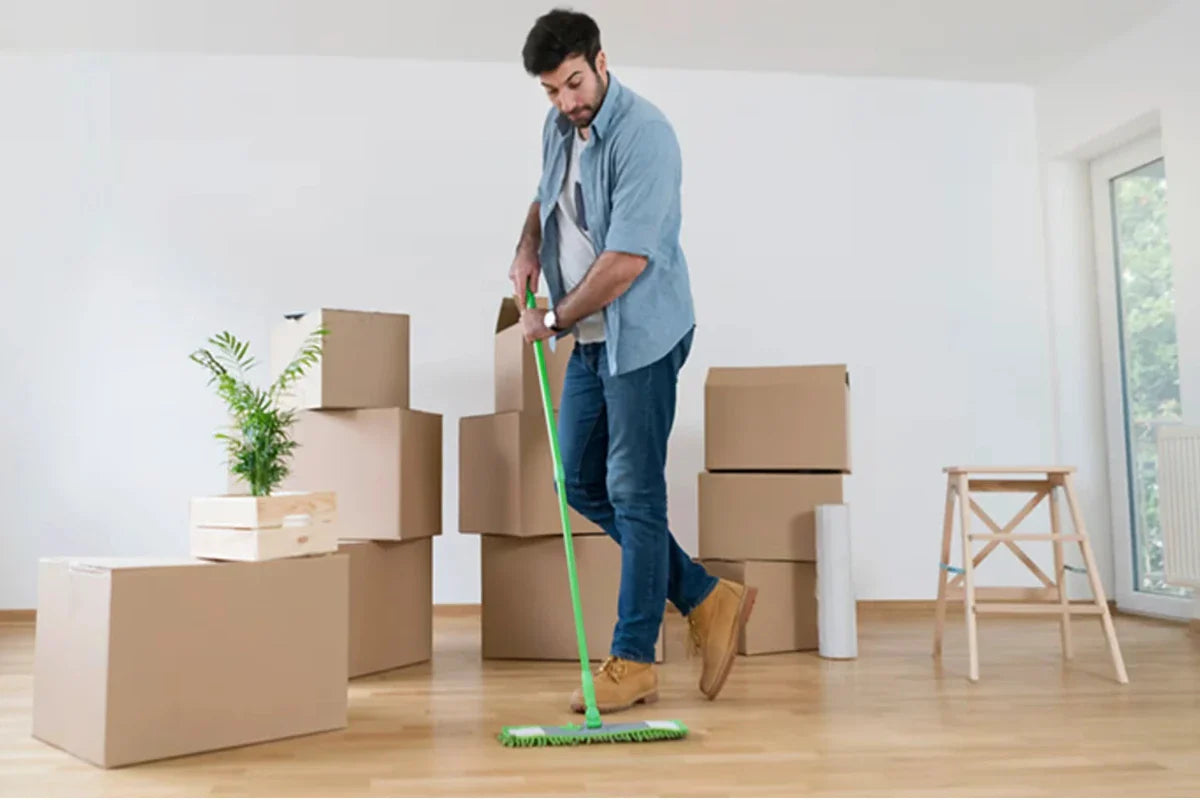 man cleaning a wooden floor in an empty house surrounded by moving boxes