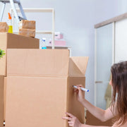 a woman moving house who is  labelling an XL cardboard box with a marker