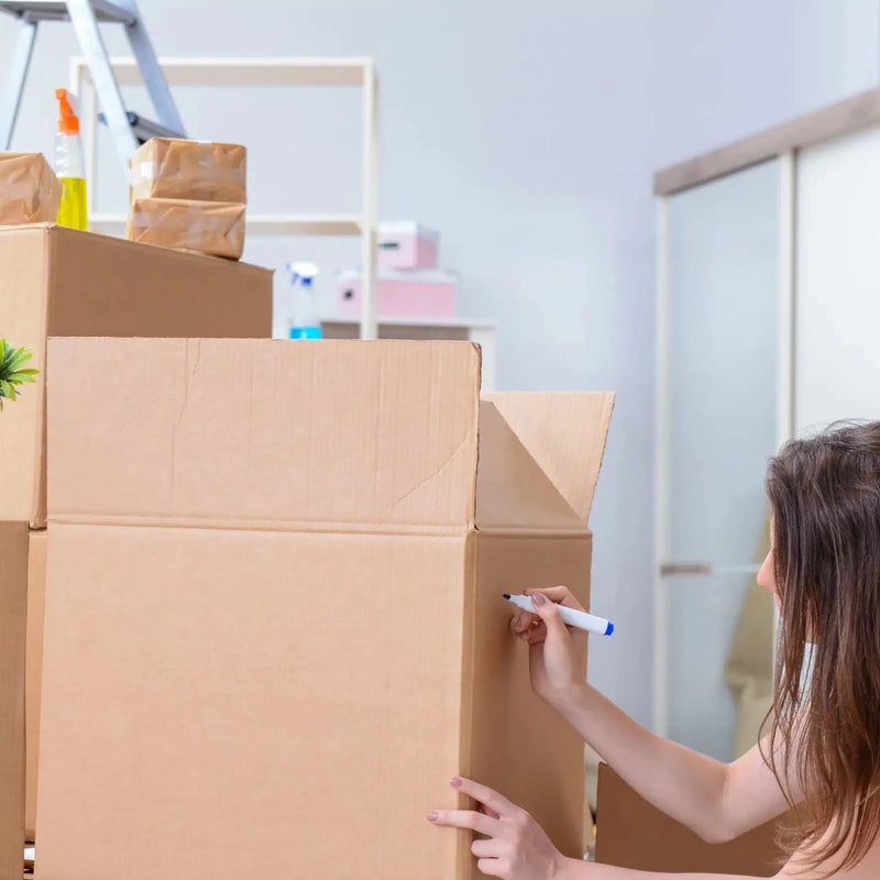 a woman moving house who is  labelling an XL cardboard box with a marker