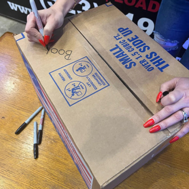 Woman writing with a black marker on a cardboard box that has been placed on a table