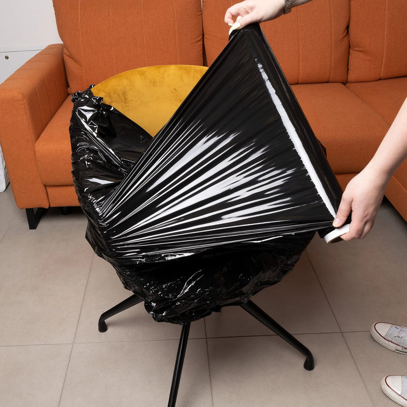 hands using a roll of black pallet wrap to wrap furniture in a living room