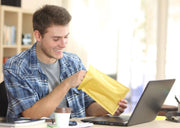 a man at an office desk opening a brown padded envelope