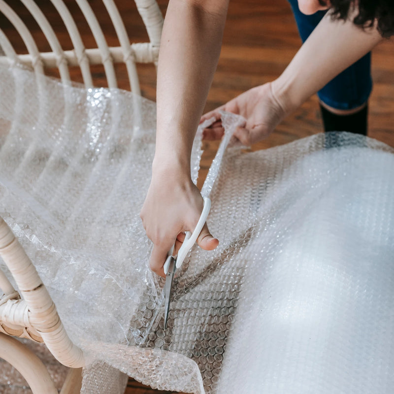 Woman wrapping a chair with bubble wrap in a living room environment