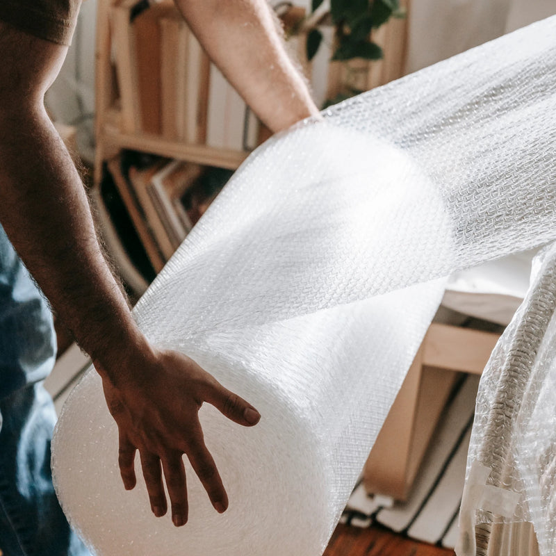 Man wrapping furniture with a 20-metre roll of clear bubble wrap in a living room environment