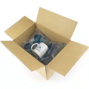 a cardboard box with a mug lying on a layer of Bubl Void 12x20 air cushioning on a white background