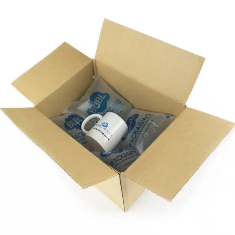 a cardboard box with a mug lying on a layer of Bubl Void 12x20 air cushioning on a white background