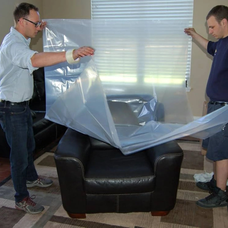 two men unpacking a clear chair bag in a living room in preparation to cover a brown leather armchair