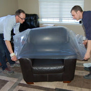 two men covering a leather armchair with a clear chair bag in a living room