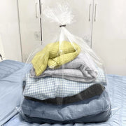a clear bedding bag filled with clothes on top of a bed with a wardrobe in the background