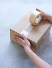 A woman taping a postal box closed using a roll of clear sealing tape on a neutral background