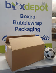 A brown cardboard box displayed on a counter in front of a white sign for boxdepot.ie, with a black and white soccer ball next to it.