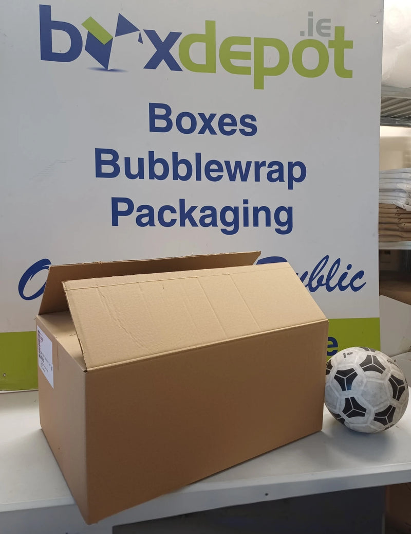 A brown cardboard box displayed on a counter in front of a white sign for boxdepot.ie, with a black and white soccer ball next to it.