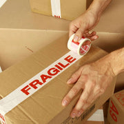 A man sealing a cardboard box by hand with fragile tape