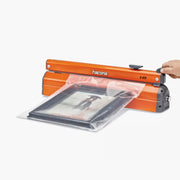 A hand sealing a framed picture in a plastic bag using a Hacona C420 Heat Sealer on a white background
