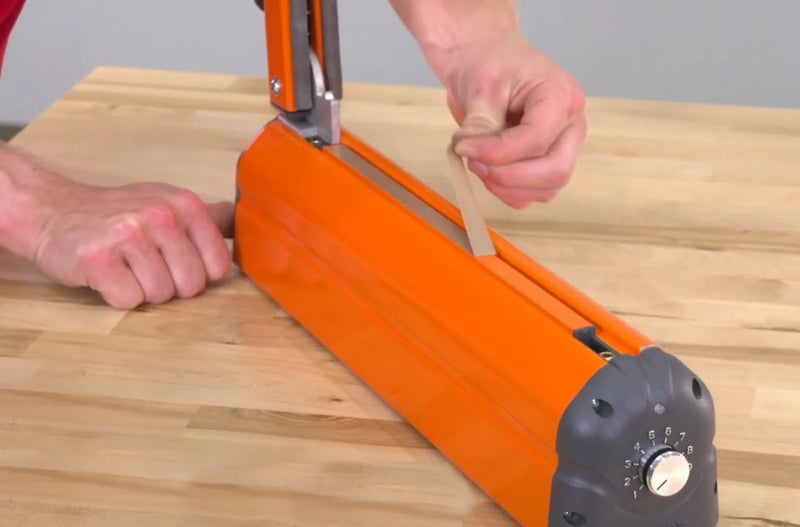 Person replacing a teflon strip on a Hacona Heat Sealer on a wooden table