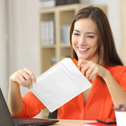 a woman taking a break from working at her laptop to open a mail lite white padded envelope