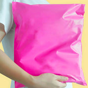 a woman holding a filled pink mailing bag on a neutral background