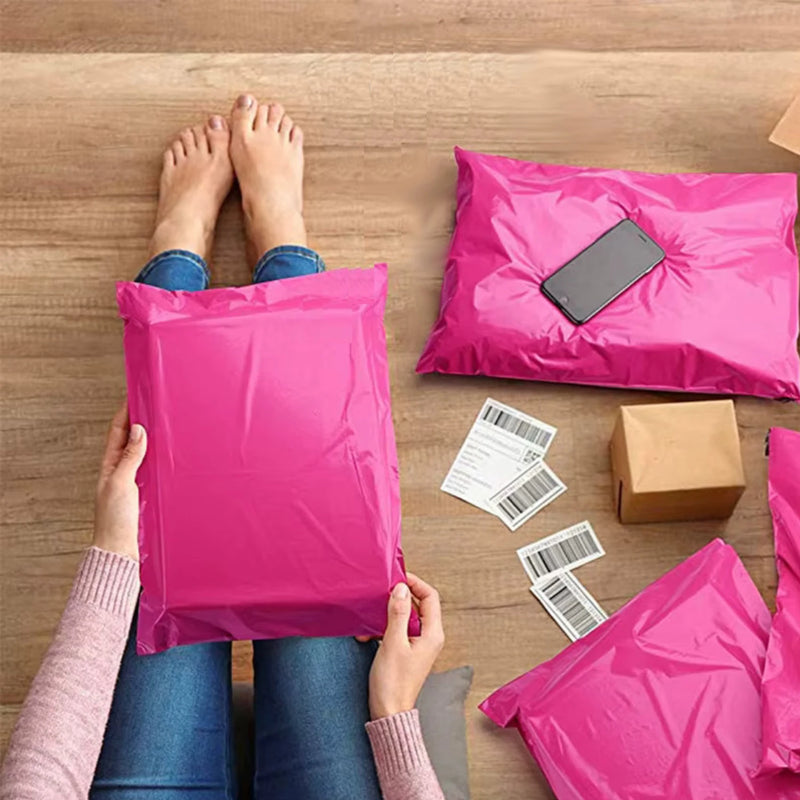 A woman sitting on a wooden floor packing products for shipping using pink mailing bags