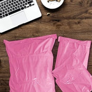 three filled pink mailing bags on a wooden desk beside a laptop computer