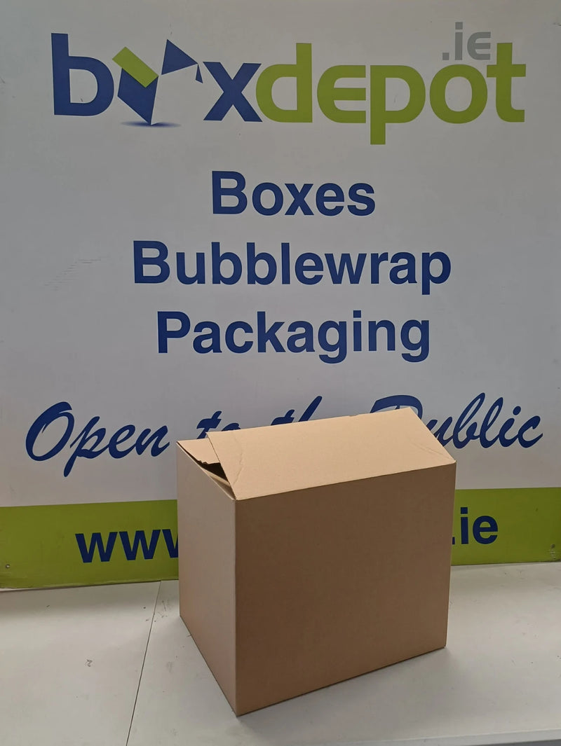 A plain brown cardboard box standing upright in front of Box Depot advertising board
