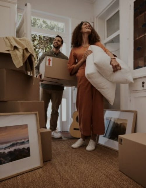 A couple carrying moving boxes and other belongings into their new house
