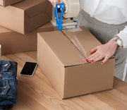 closeup of a woman sealing a cardboard box with sealing tape on a table
