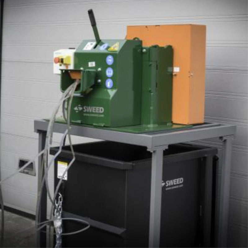 Sweed CE510 Strapping Chopper on a metal table with a plastic skip bin below while the machine is being fed with plastic pallet strapping in a warehouse
