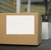 A blank white address label on a brown cardboard box in a warehouse