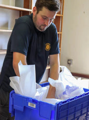 a man packing items into a plastic crate using acid free tissue in a home environment suggesting he is moving house