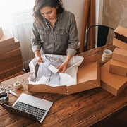 a  woman packing a shirt into a cardboard box using acid free tissue paper in an office environment