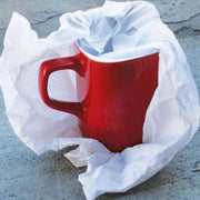 a sheet of acid free tissue paper wrapped around a red mug on a slate background