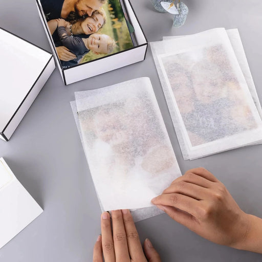 woman wrapping photographs in acid free tissue on a gray surface with a photo in the background