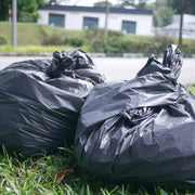 filled and closed black bin bags on grass beside an outdoor road