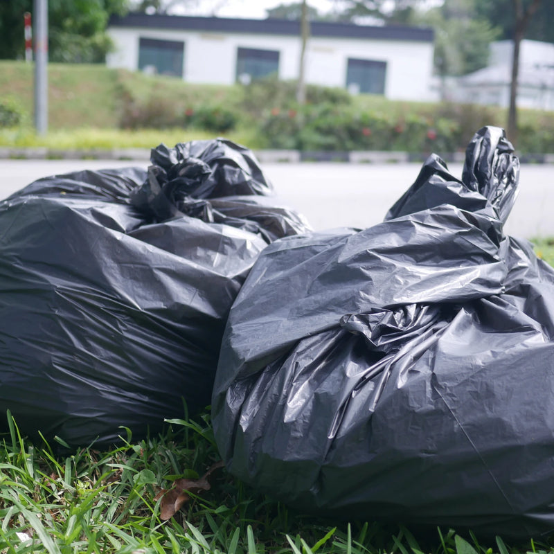 filled and closed black bin bags on grass beside an outdoor road