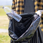 Man holding a open black bin bag, putting an empty plastic bottle into it in an outdoor environment