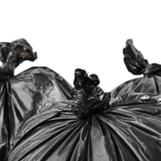 closeup of three black bin bags that have been knotted closed on a white background