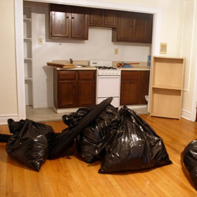 a number of filled black bin bags on the floor of an emptied kitchen