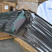 closeup of a man stretching black pallet wrap to show how it resists puncture in a warehouse