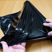 Close up image of a man trying to stretch black pallet wrap with his hand