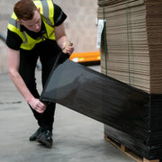 Man wrapping a pallet of cardboard with black pallet wrap in an industrial setting