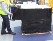 a man wearing a hi-viz jacket wrapped a full pallet in black pallet wrap in a warehouse