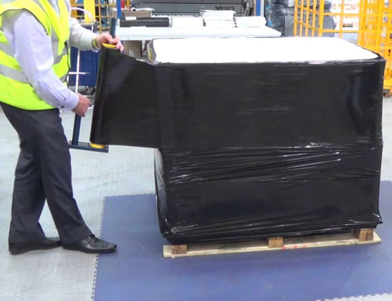a man wearing a hi-viz jacket wrapped a full pallet in black pallet wrap in a warehouse