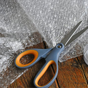 Scissors with orange handles on a wooden surface with bubble wrap