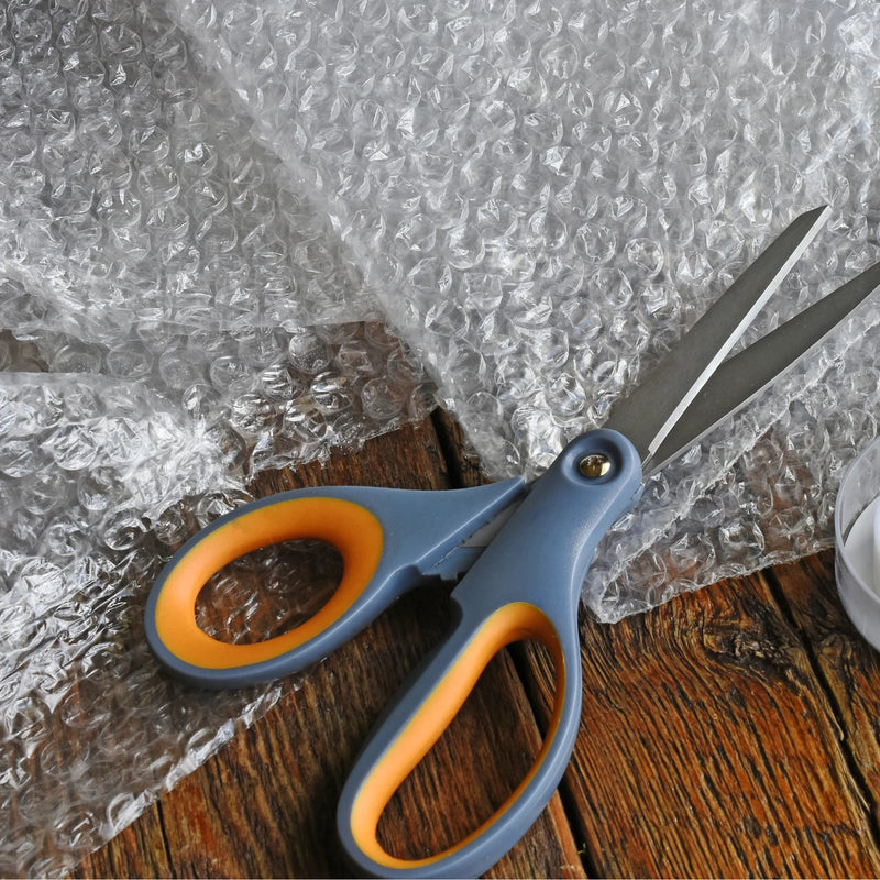 Scissors with orange handles on a wooden surface with bubble wrap