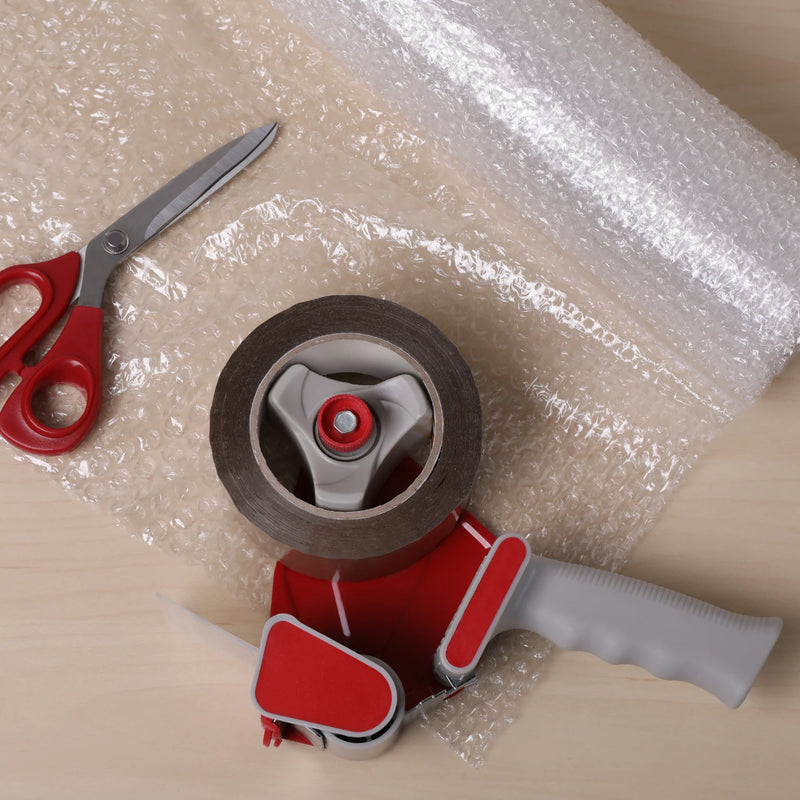 Tape dispenser, scissors, and roll of bubble wrap on a plain tabletop