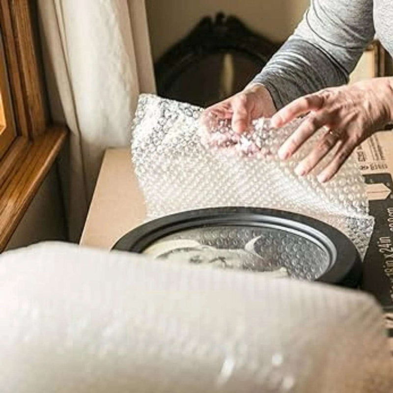 An elderly woman using bubble wrap to protect framed photographs when moving house