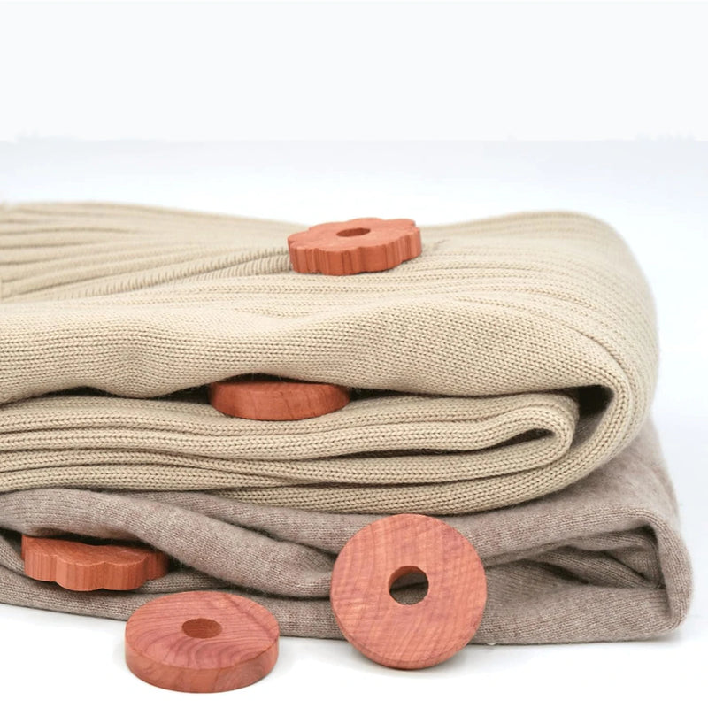 Folded woolly jumpers interspersed with cedar moth repellent rings on a white background