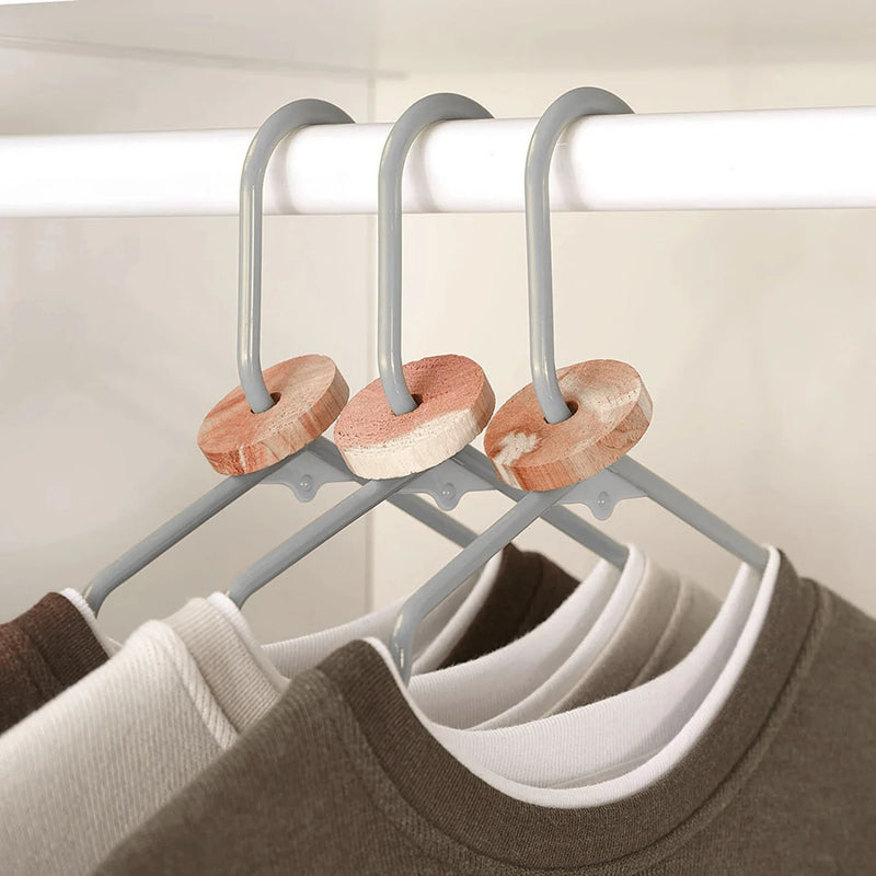 Set of three hangers with cedar moth repellent rings on a wardrobe rail.