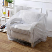 White armchair covered with clear armchair cover bag in a room with wooden floor and white walls.